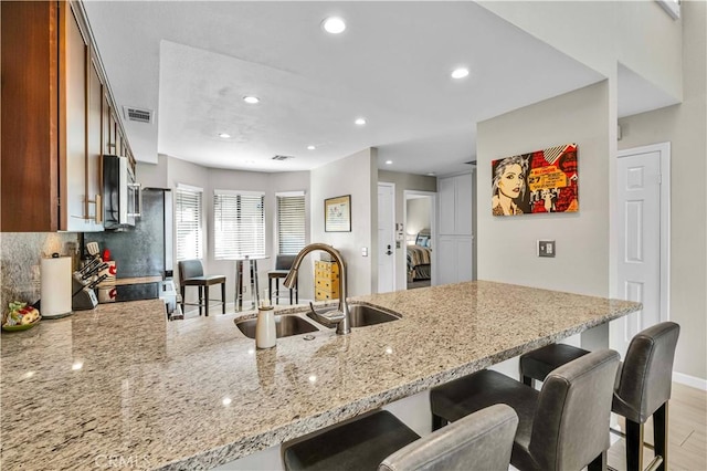 kitchen featuring sink, light stone counters, light hardwood / wood-style flooring, kitchen peninsula, and decorative backsplash