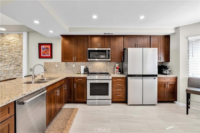 kitchen with sink, appliances with stainless steel finishes, tasteful backsplash, light stone countertops, and kitchen peninsula