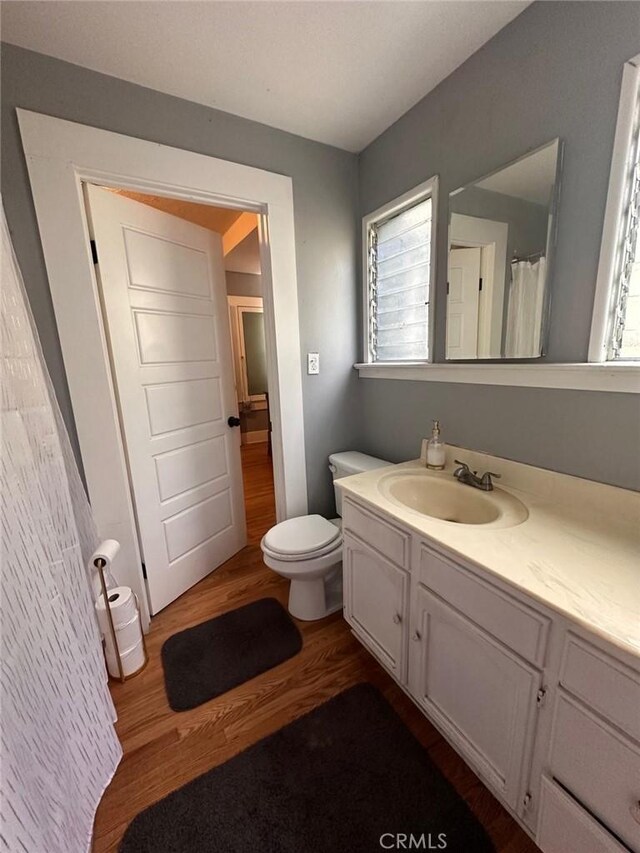 full bathroom with plenty of natural light, vanity, toilet, and wood finished floors