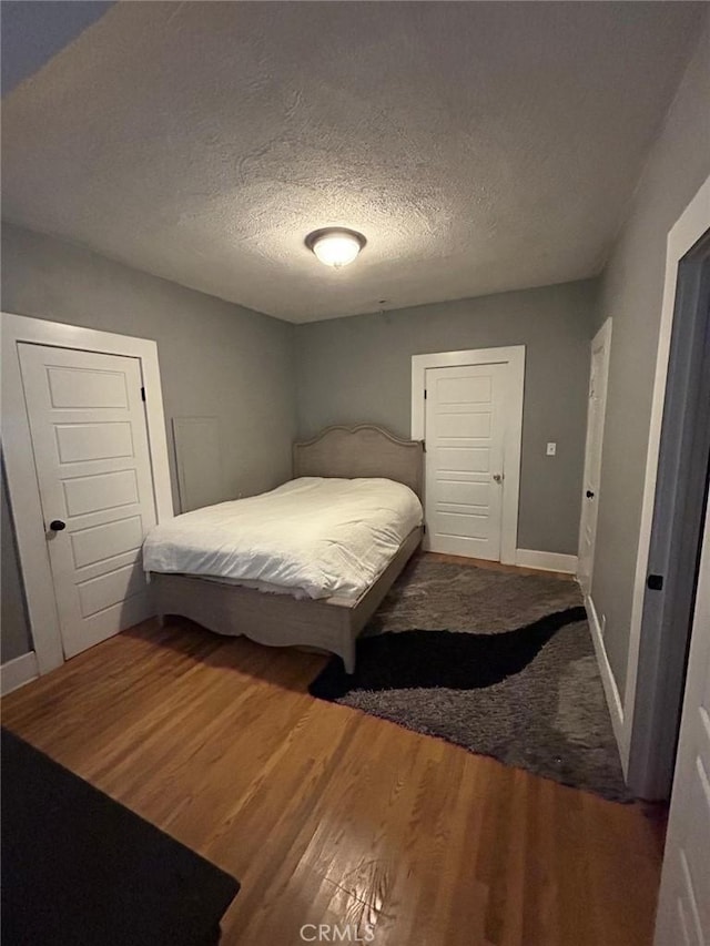 bedroom with a textured ceiling, baseboards, and wood finished floors