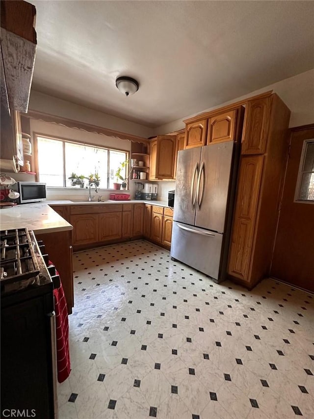 kitchen featuring brown cabinets, light floors, light countertops, appliances with stainless steel finishes, and a sink