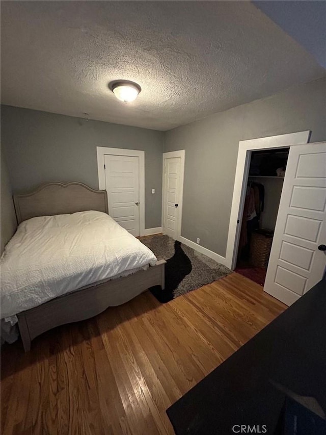 bedroom with a textured ceiling, a closet, baseboards, and wood finished floors