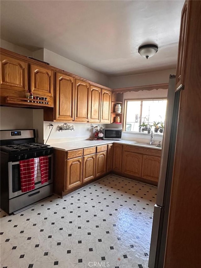 kitchen featuring light floors, light countertops, appliances with stainless steel finishes, brown cabinetry, and a sink