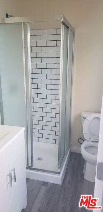 bathroom featuring wood-type flooring, toilet, vanity, and walk in shower