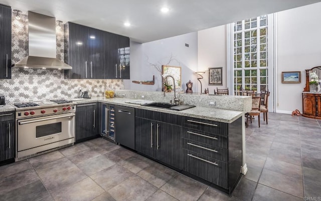 kitchen featuring wall chimney range hood, sink, light stone counters, designer range, and kitchen peninsula