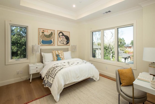 bedroom with multiple windows, hardwood / wood-style floors, ornamental molding, and a raised ceiling