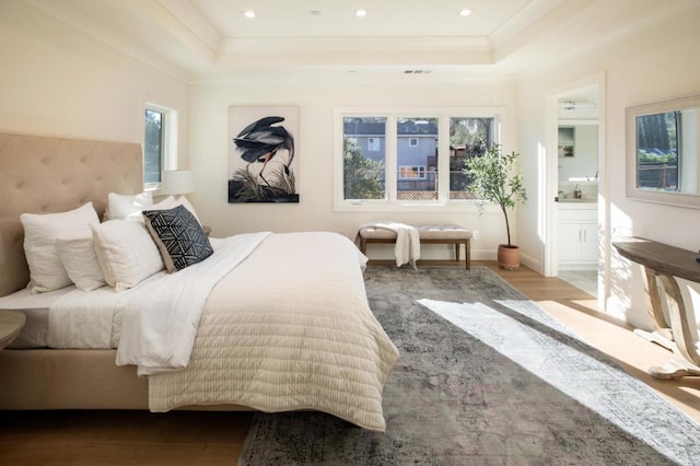 bedroom with ensuite bath, ornamental molding, a raised ceiling, and light wood-type flooring