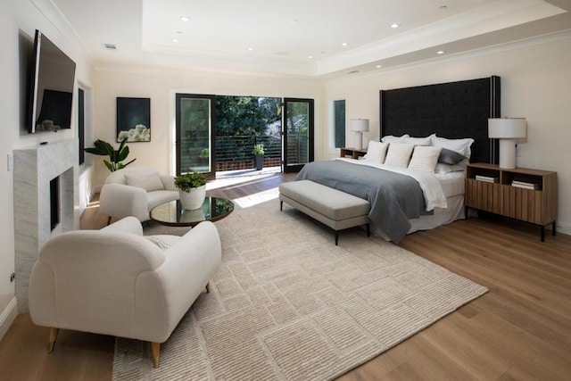 bedroom featuring a tray ceiling, a high end fireplace, ornamental molding, and wood-type flooring