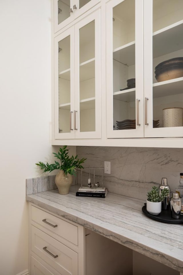 bar with light stone counters, tasteful backsplash, and white cabinets