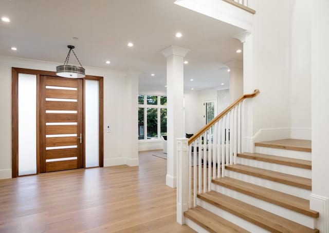 entrance foyer featuring crown molding, light hardwood / wood-style floors, and ornate columns