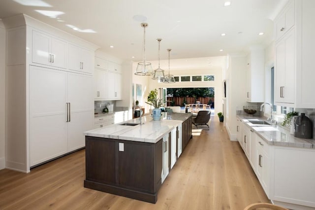 kitchen featuring a spacious island, white cabinetry, decorative light fixtures, and sink