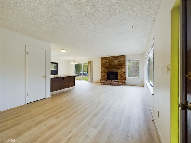 unfurnished living room featuring a notable chandelier, a textured ceiling, a brick fireplace, and light wood-type flooring