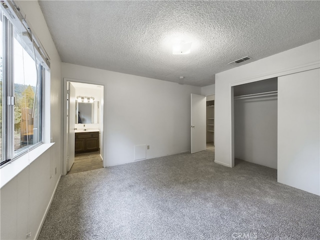 unfurnished bedroom featuring ensuite bathroom, light carpet, a textured ceiling, and a closet