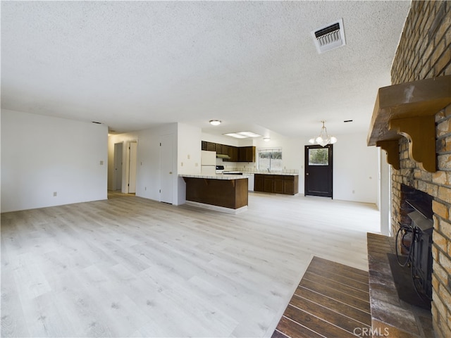 unfurnished living room with wood-type flooring, a chandelier, a textured ceiling, and a fireplace