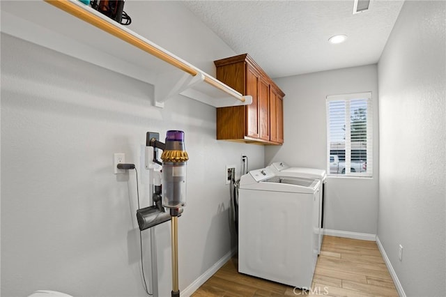 laundry room with cabinets, washing machine and dryer, a textured ceiling, and light hardwood / wood-style floors