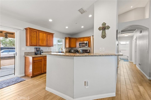 kitchen with lofted ceiling, appliances with stainless steel finishes, light stone countertops, and light hardwood / wood-style flooring