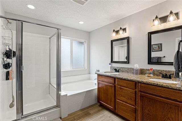 bathroom featuring wood-type flooring, separate shower and tub, vanity, and a textured ceiling