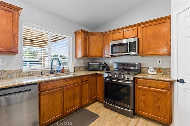 kitchen featuring lofted ceiling, sink, light stone counters, and appliances with stainless steel finishes