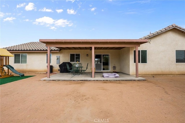 back of property featuring a playground and a patio