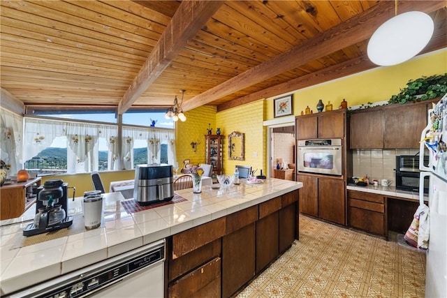 kitchen featuring pendant lighting, stainless steel oven, dark brown cabinetry, and tile counters