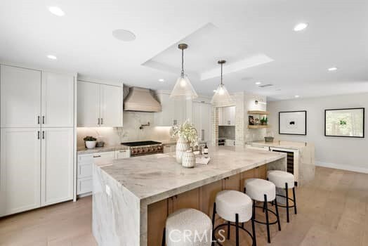 kitchen featuring hanging light fixtures, a spacious island, light stone counters, white cabinets, and wall chimney exhaust hood