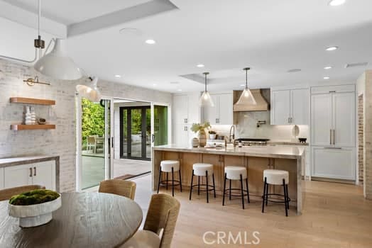 kitchen with a kitchen bar, white cabinetry, decorative light fixtures, a kitchen island with sink, and wall chimney range hood