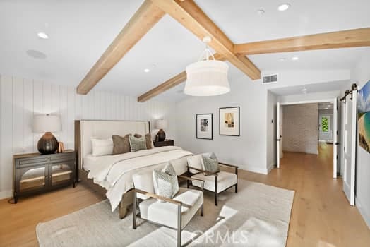 bedroom with vaulted ceiling with beams, light hardwood / wood-style flooring, and a barn door