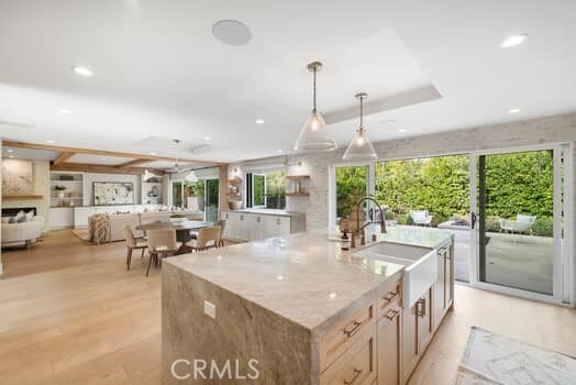 kitchen with a large island, sink, light stone counters, decorative light fixtures, and light wood-type flooring