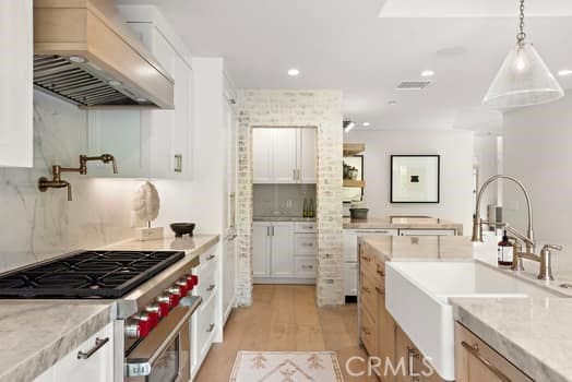 kitchen featuring pendant lighting, sink, high end stove, custom range hood, and white cabinets