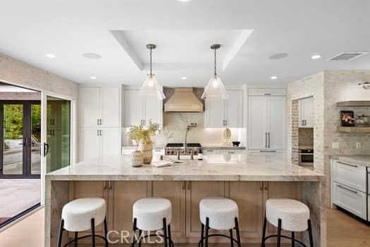 kitchen with premium range hood, light stone countertops, a center island with sink, and white cabinets