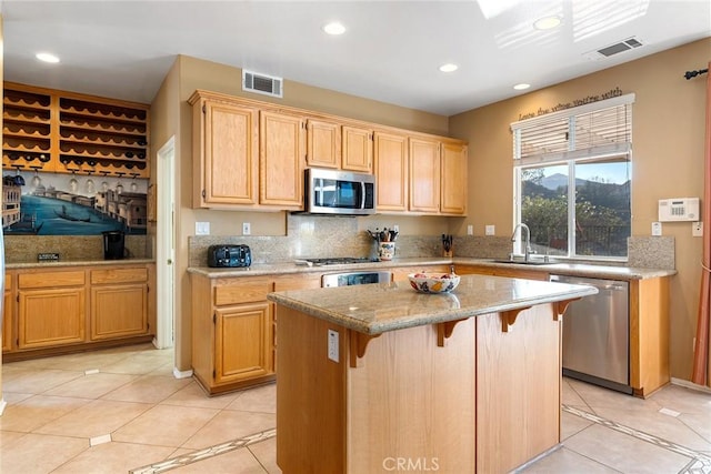 kitchen featuring sink, a center island, light tile patterned floors, stainless steel appliances, and light stone countertops