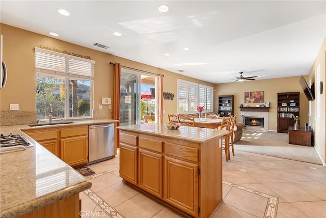 kitchen with light tile patterned floors, ceiling fan, appliances with stainless steel finishes, a fireplace, and a kitchen island