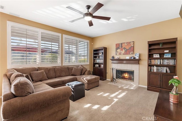 living room with a tile fireplace, light colored carpet, and ceiling fan