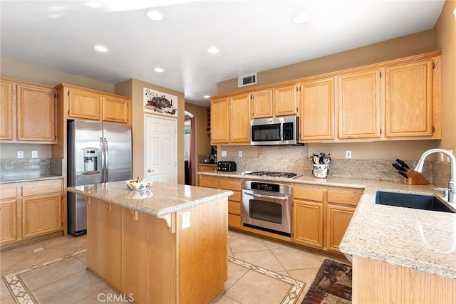 kitchen with light tile patterned flooring, a kitchen island, appliances with stainless steel finishes, sink, and light stone countertops