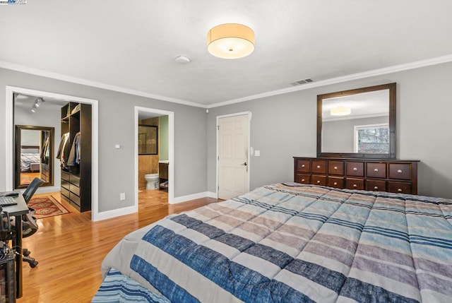 bedroom with crown molding, a walk in closet, wood-type flooring, and connected bathroom