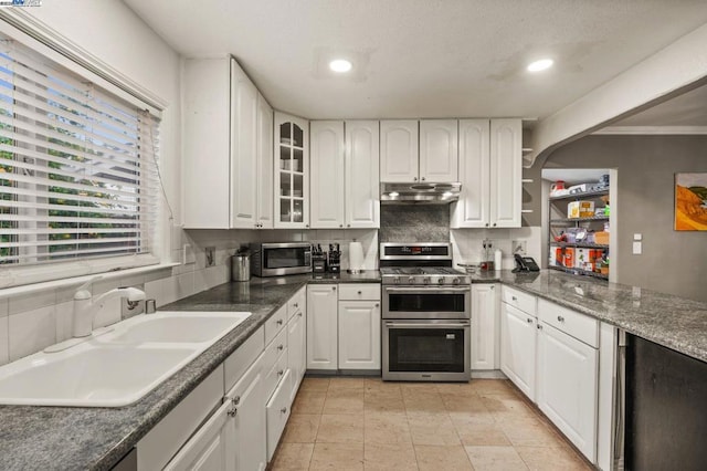 kitchen featuring sink, appliances with stainless steel finishes, white cabinetry, backsplash, and dark stone countertops