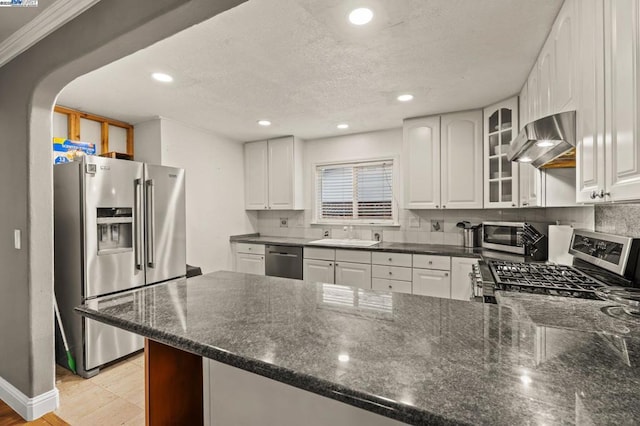 kitchen with appliances with stainless steel finishes, white cabinetry, backsplash, range hood, and kitchen peninsula