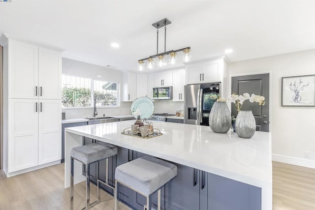 kitchen featuring a breakfast bar area, decorative light fixtures, a center island, appliances with stainless steel finishes, and white cabinets