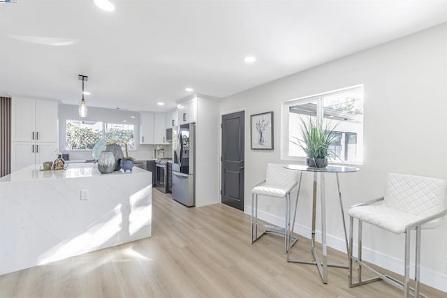 kitchen with light hardwood / wood-style flooring, white cabinetry, hanging light fixtures, stainless steel appliances, and light stone counters