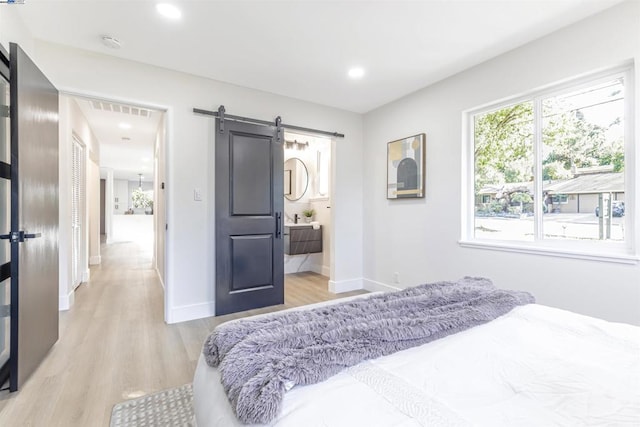 bedroom featuring connected bathroom, a barn door, and light hardwood / wood-style floors