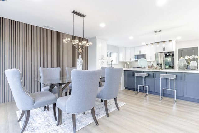 dining area with sink, light hardwood / wood-style floors, and a notable chandelier