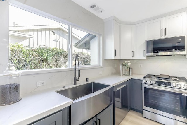 kitchen featuring appliances with stainless steel finishes, sink, white cabinets, backsplash, and light wood-type flooring