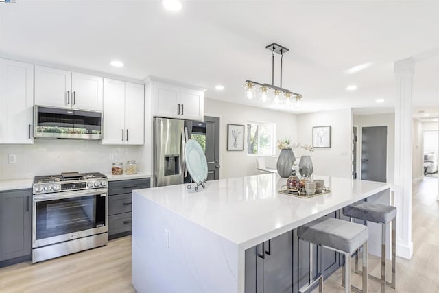 kitchen with white cabinetry, stainless steel appliances, hanging light fixtures, and a kitchen island