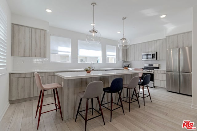 kitchen with light brown cabinetry, decorative light fixtures, appliances with stainless steel finishes, a kitchen island, and decorative backsplash