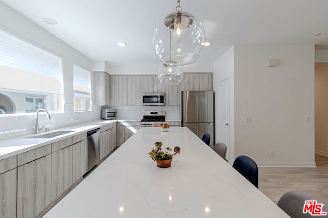 kitchen with appliances with stainless steel finishes, decorative light fixtures, sink, light stone counters, and light hardwood / wood-style flooring