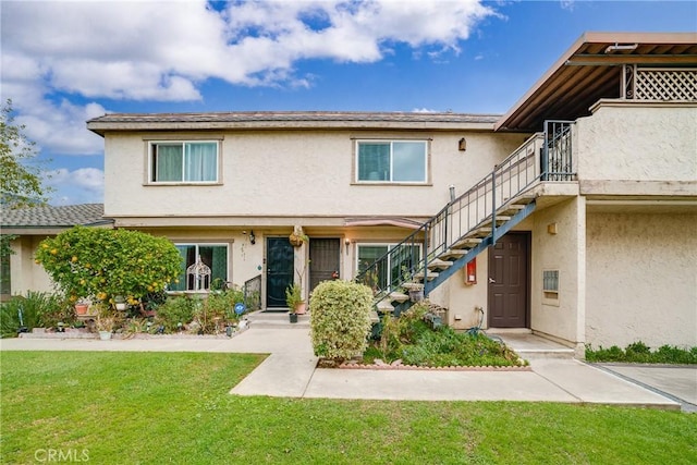 townhome / multi-family property with stairs, a front lawn, and stucco siding