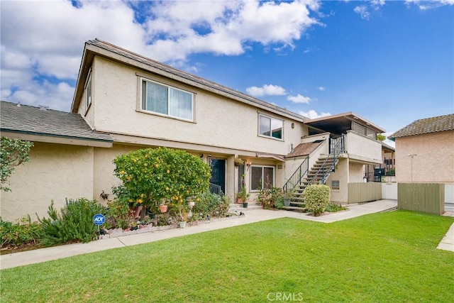 view of front of home featuring stucco siding, stairway, and a front yard