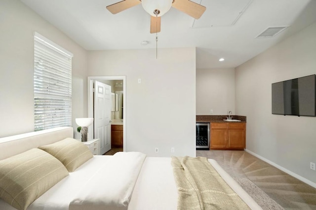 carpeted bedroom with connected bathroom, indoor wet bar, beverage cooler, and ceiling fan