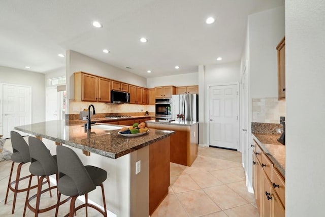 kitchen with sink, a breakfast bar area, dark stone counters, stainless steel appliances, and a center island with sink