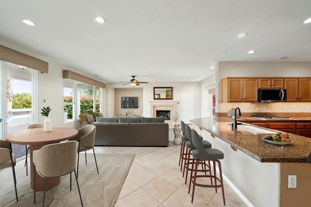 kitchen with a breakfast bar area, appliances with stainless steel finishes, dark stone countertops, light tile patterned flooring, and decorative backsplash